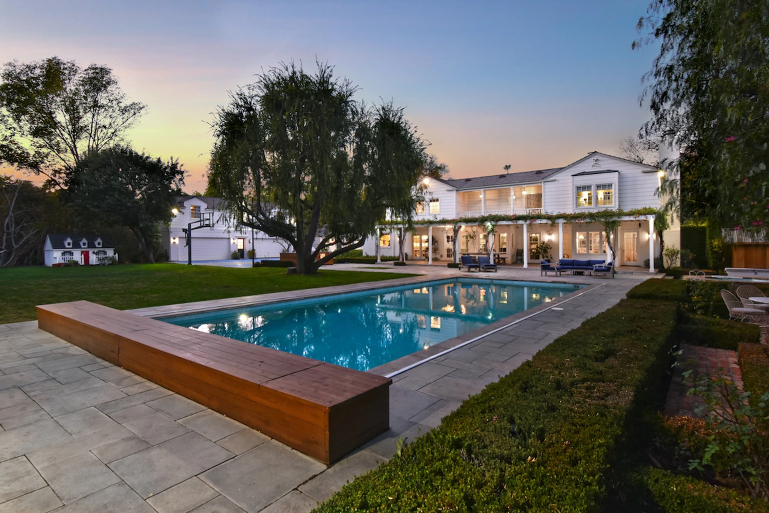 Listing photo of a white two-storey house at dusk, seen across a lit swimming pool