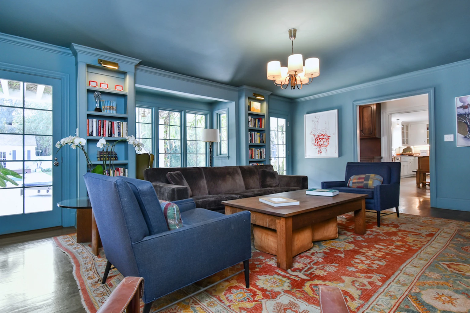 Listing photo of a blue-walled living room with a chandelier, built-in bookshelves and a patterned rug